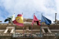 Áreas de Práctica From below of Spanish flag and flags of Spanish provinces together with European Union flag waving on facade of magnificent stone building on sunny day